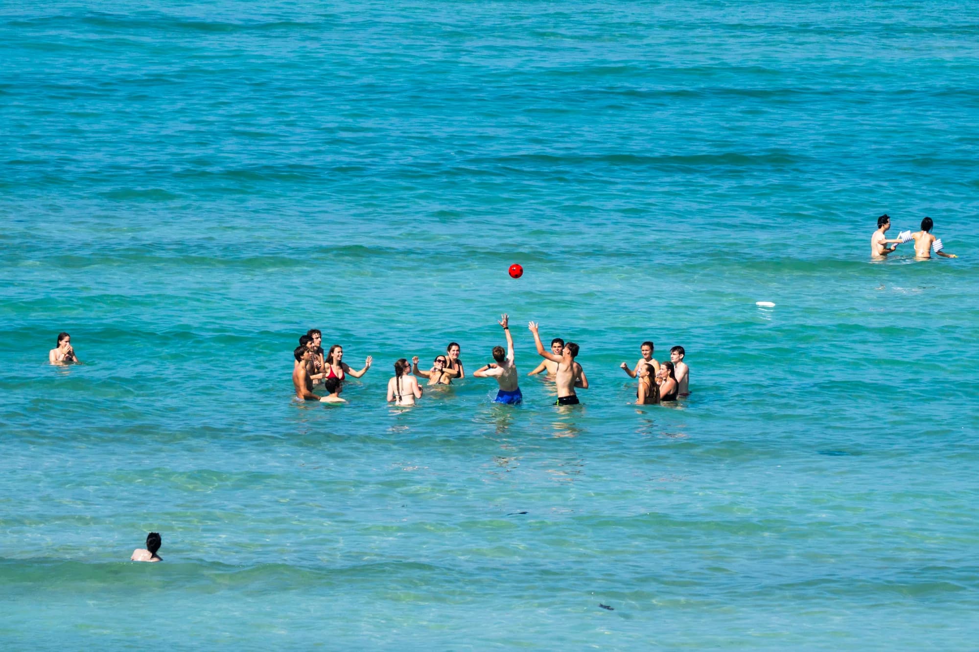 Photo by Zechariah: swimmers tossing a red ball in turquoise water