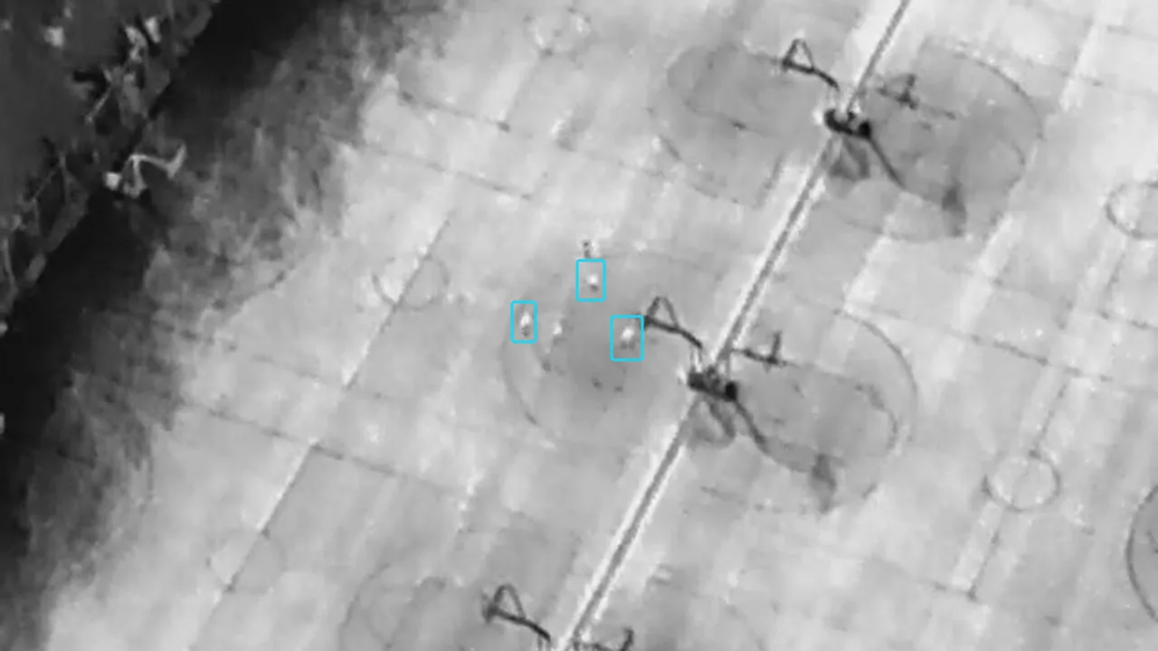 Thermal drone image of a basketball court with three people outlined by their labeled bounding boxes